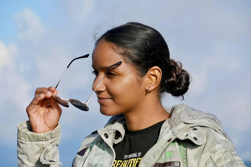 Young woman holding sunglasses with sky background